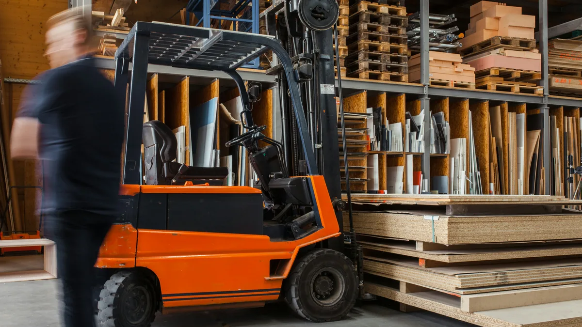 Heftruck in een magazijn terwijl een medewerker er vlak langs loopt