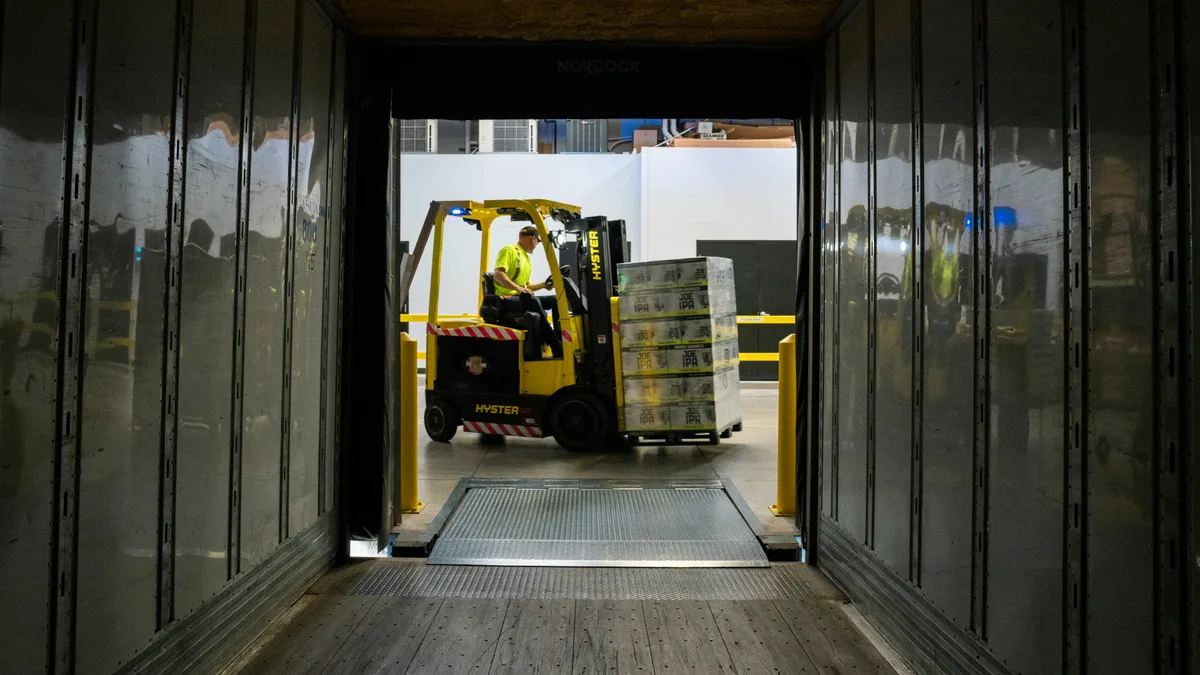 Heftruck met pallet bij een laaddock terwijl een collega in de buurt werkt